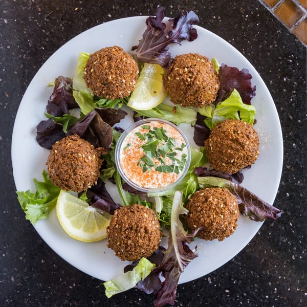 A white plate of falafel, lettuce, lemon wedges, and a dipping sauce with parsley and paprika.