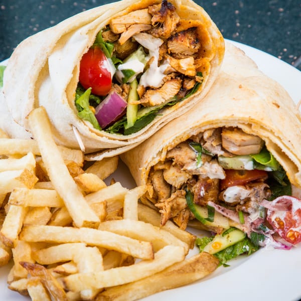 Two chicken shawarma wraps with fresh vegetables and white sauce, served with golden french fries.