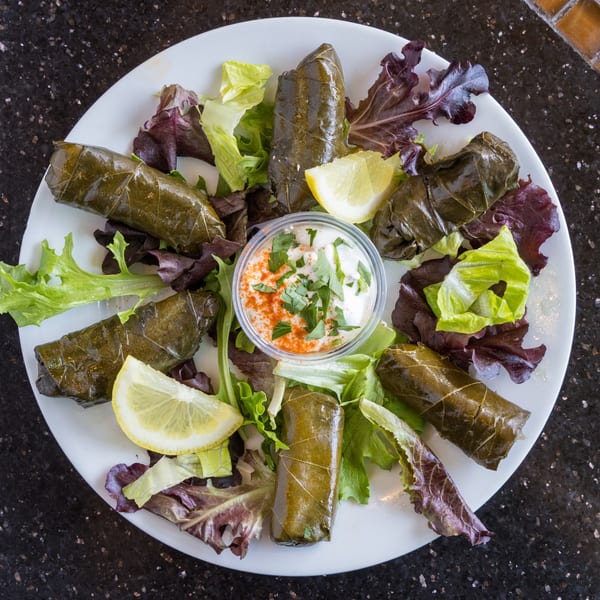 Plate of dolmades (stuffed grape leaves) with lettuce, lemon wedges, and a side of dipping sauce.