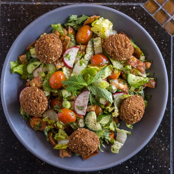 Overhead view of a vibrant falafel salad with cherry tomatoes, radishes, cucumbers, and mint.