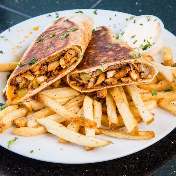 Two chicken shawarma wraps, cut in half, served with french fries and a side of white sauce.