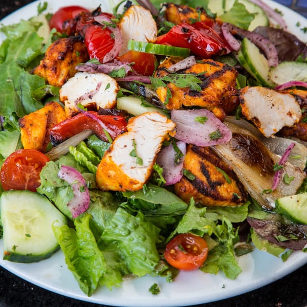 Grilled chicken and vegetable salad with lettuce, tomatoes, cucumbers, and red onions on a white plate.